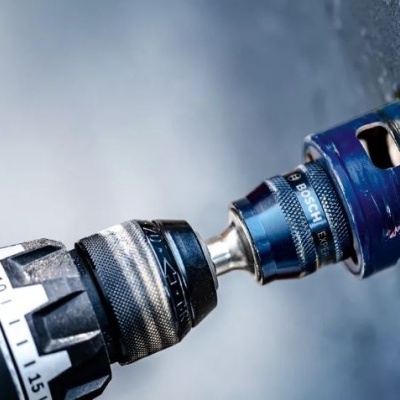 Broca elétrica a furar numa superfície com caixa azul e mandril preto e cinzento