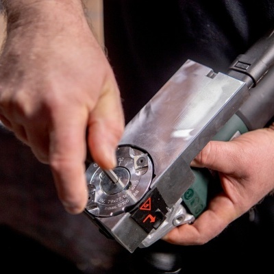 Ferramenta elétrica metálica e verde sendo ajustada por mãos em ambiente de trabalho