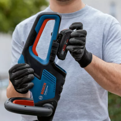 Serra de corrente Bosch azul, detalhes laranja e preto, segurada por pessoa com luvas pretas e t-shirt cinza em exterior