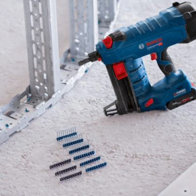 Pistola de pregos azul e preta BOSCH Professional com pregos no chão em ambiente de construção