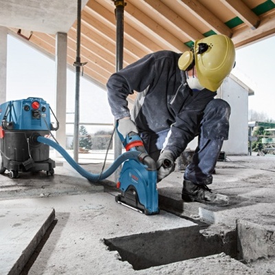 Trabalhador a cortar laje de cimento com serra elétrica azul num canteiro de obras