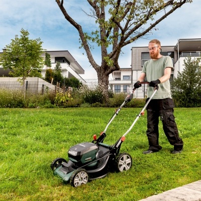 Homem a cortar relva com cortador de relva elétrico num jardim