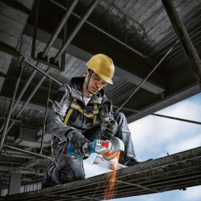 Trabalhador com capacete e luvas usando rebarbadora em estrutura metálica