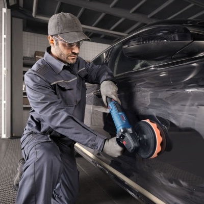 Homem a polir carro preto com polidora elétrica numa oficina