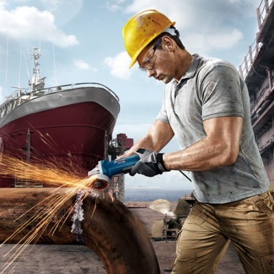 Homem com capacete amarelo a usar esmerilhadora elétrica em tubo de metal no estaleiro