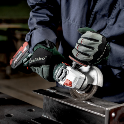 Esmerilhadeira Metabo a cortar peça metálica, mãos com luvas de proteção, fundo de oficina.