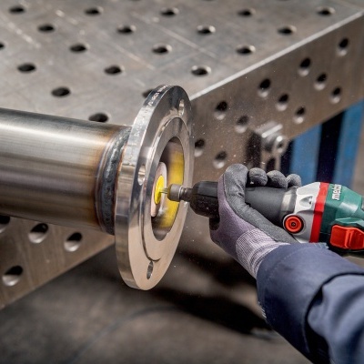 Pessoa a polir uma peça metálica cilíndrica com ferramenta elétrica