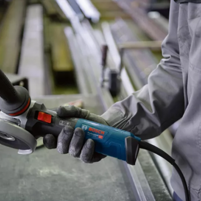 Pessoa segura rebarbadora elétrica BOSCH azul em oficina com luvas cinzentas