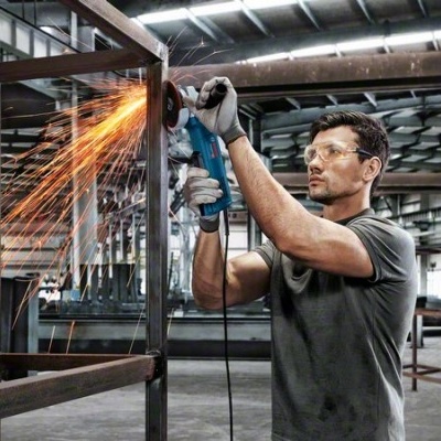 Homem a usar rebarbadora em estrutura metálica numa oficina industrial