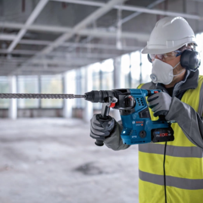 Trabalhador com capacete e colete a usar ferramenta elétrica para perfurar parede