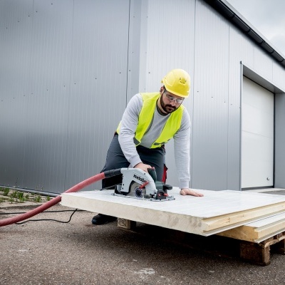 Homem a cortar placa de madeira com ferramenta elétrica em ambiente industrial