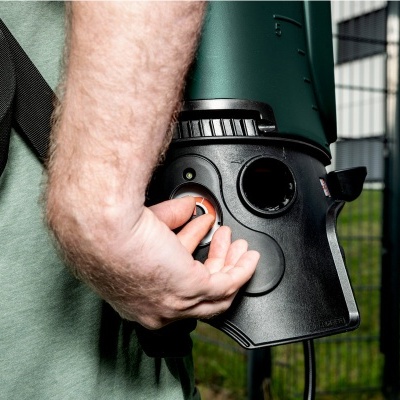 Pessoa a segurar ferramenta eléctrica verde com botão laranja perto de vedação metálica