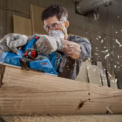 Homem a usar plaina elétrica azul Bosch numa oficina de madeira