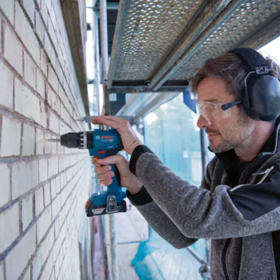 Homem usando furadeira Bosch para perfurar parede de tijolos