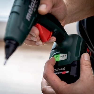 Pistola de cola quente Metabo verde escuro com detalhes vermelhos nas mãos