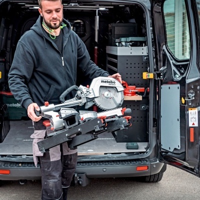Homem a carregar serra Metabo de corte junto a carrinha preta com portas traseiras abertas
