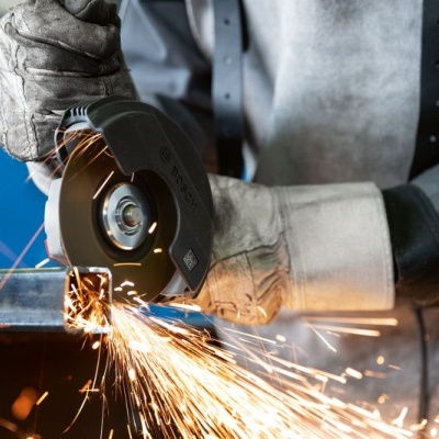 Pessoa usando luvas e avental operando rebarbadora elétrica gerando faíscas