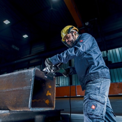 Homem a trabalhar com ferramenta elétrica numa estrutura metálica grande num ambiente industrial.