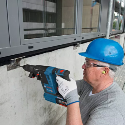 Homem com capacete azul a usar furadeira sem fio numa parede de construção