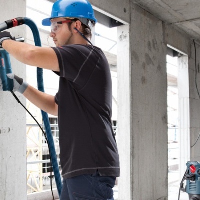 Homem com capacete azul a usar ferramenta elétrica para perfuração em construção