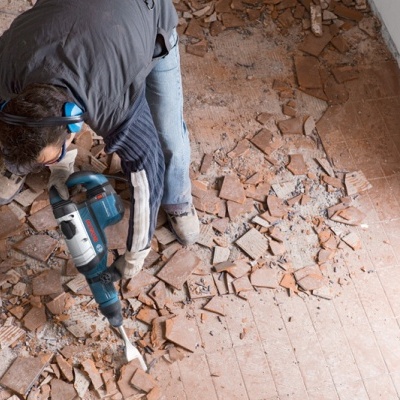 Pessoa a partir chão de azulejos castanhos com martelo demolidor