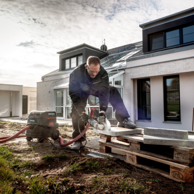 Trabalhador a cortar placa com serra elétrica em frente a casa moderna branca