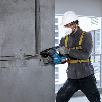 Homem com equipamento de proteção a usar martelete elétrico em parede de cimento.