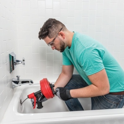 Homem a usar desentupidora na banheira numa casa de banho branca
