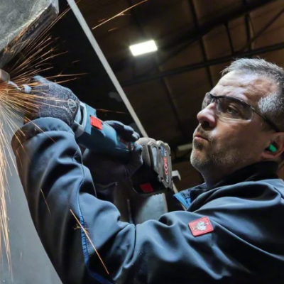 Homem a cortar chapa metálica preta com esmeriladora em ambiente industrial