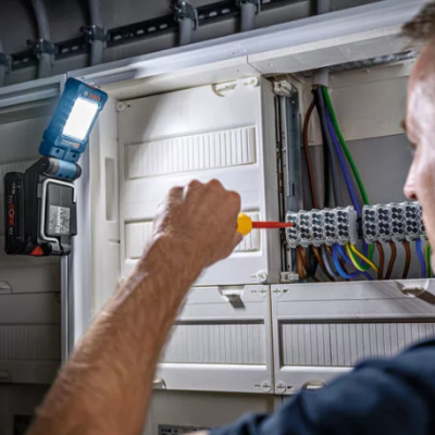 Lanterna LED azul e preta num painel elétrico com homem a trabalhar