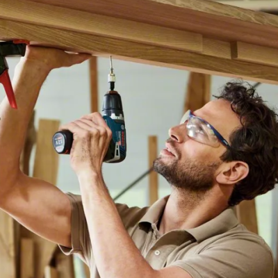 Homem a montar estrutura de madeira com furadeira e prensas