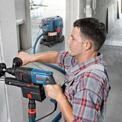Homem a usar broca elétrica Bosch com aspirador industrial ao fundo em obra