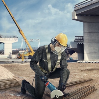 Trabalhador de construção com equipamento de proteção a cortar aço numa obra.