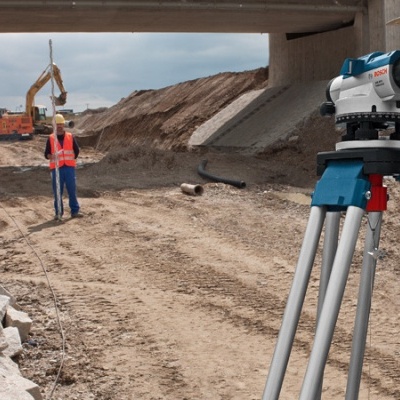 Trabalhadores de construção num canteiro com equipamento de medição e maquinaria ao fundo