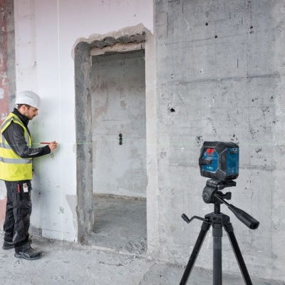 Tripé com ferramenta laser e trabalhador a medir parede no interior de construção