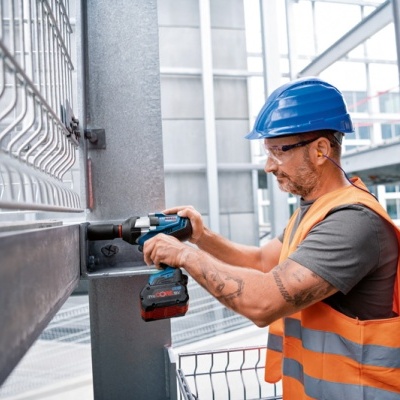 Homem com colete refletor e capacete a usar broca elétrica em estrutura metálica