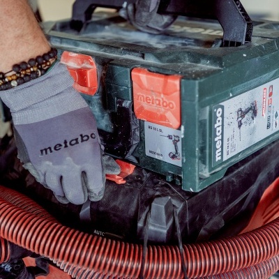 Caixa de ferramenta Metabo verde e preta com mangueira vermelha e mão com luva cinza Metabo
