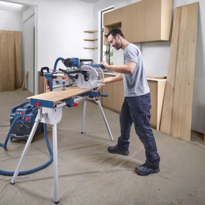 Homem a usar serra circular Bosch para cortar madeira numa bancada num espaço interior branco com tábuas de madeira