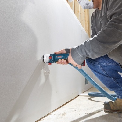 Homem usando ferramenta eléctrica azul para pintar parede branca