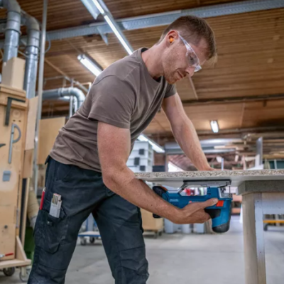 Homem a usar ferramenta elétrica numa oficina com ferramentas na parede.