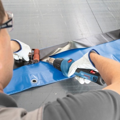 Pessoa a soldar tecido azul e preto com ferramenta e pistola de ar quente