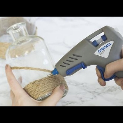 Pistola de cola quente DREMEL a aplicar cola numa garrafa de vidro com corda.