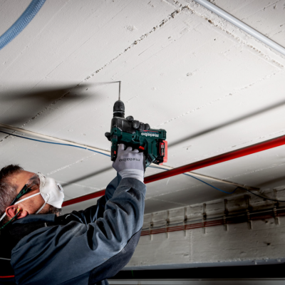 Homem a usar furadeira para fixar tubo vermelho no teto branco