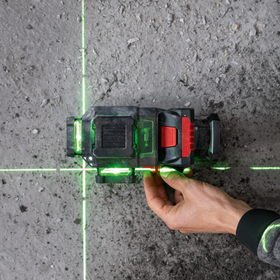 Nível laser verde com base preta e vermelha em chão cinzento, mão a ajustar