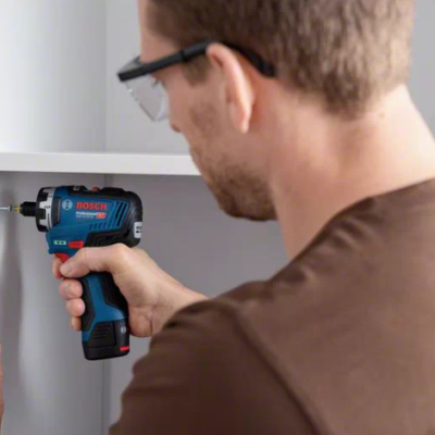 Parafusadora Bosch a bateria azul e preta em uso num armário branco