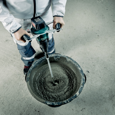 Misturadora elétrica a mexer argamassa numa bacia preta de plástico sobre chão cinzento