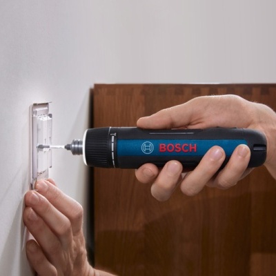 Ferramenta elétrica Bosch aparafusando suporte transparente na parede branca.