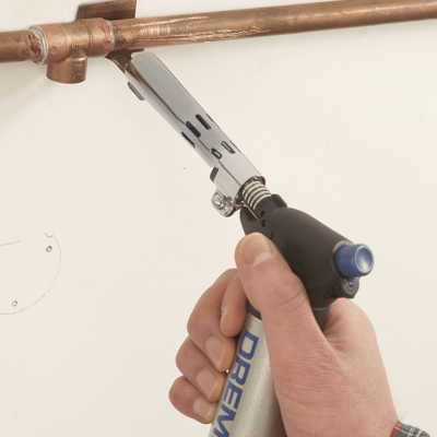 Mão usando ferramenta Dremel aquecendo tubagem de cobre na parede