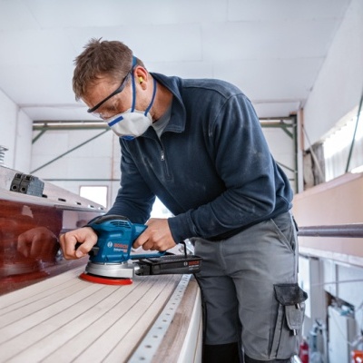 Homem usa lixadora elétrica Bosch numa superfície de madeira