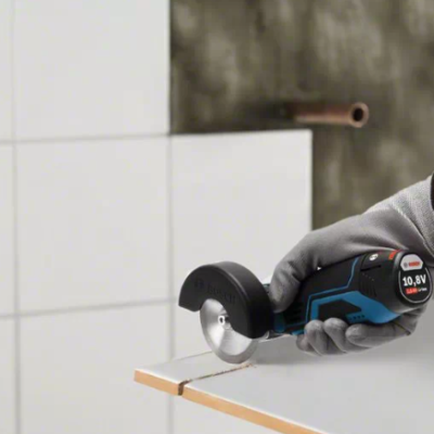 Ferramenta elétrica azul e preta a cortar prancha branca com mão luvada